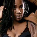 femme noire avec un regard profond. portant nuisette noire avec un léger decoletté et une veste marron