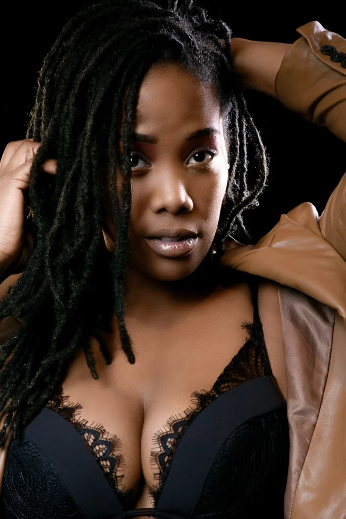 Portrait artistique d'une femme aux dreadlocks portant de la lingerie en dentelle noire et une veste en cuir marron, regardant fixement
